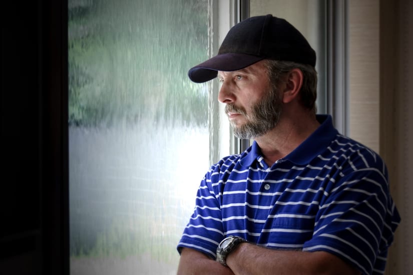 Middle Aged Man Looking Pensively Out A Window At Home