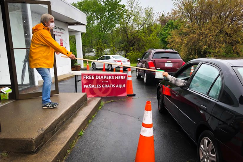 Peter Burnett wearing mask and rain jacket handing someone in car food for the Ampersand Pantry Project